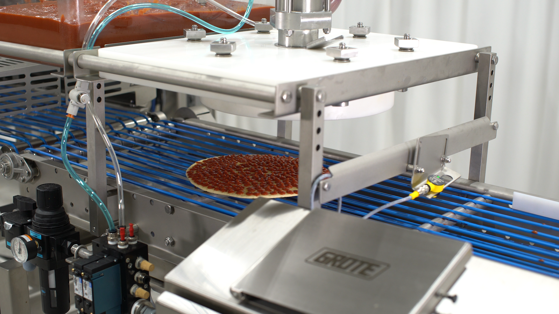 A pizza with sauce moving through a sauce applicator machine.