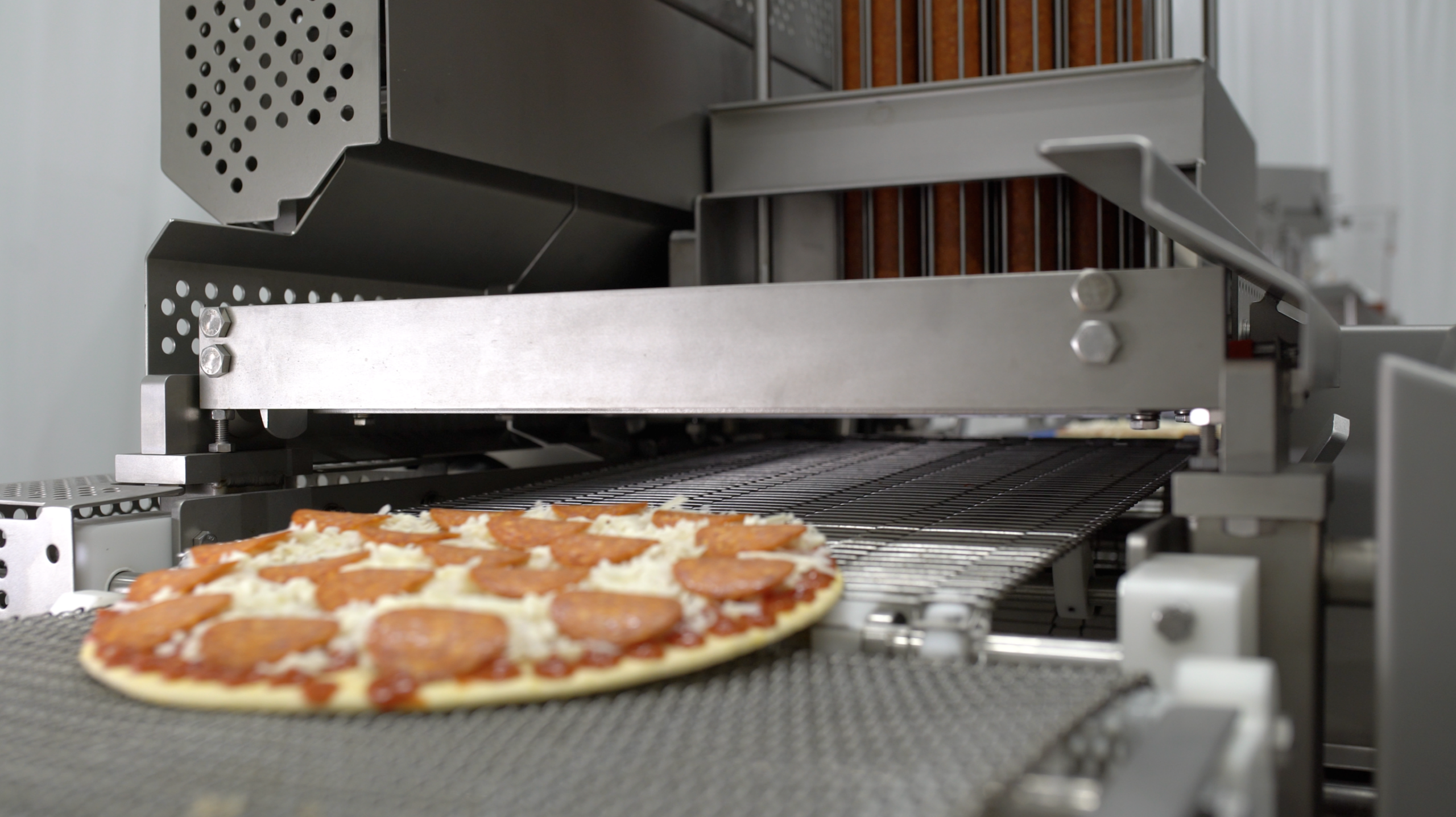 A completed frozen pizza emerges from a pepperoni slicer A completed frozen pizza emerges from a pepperoni slicer