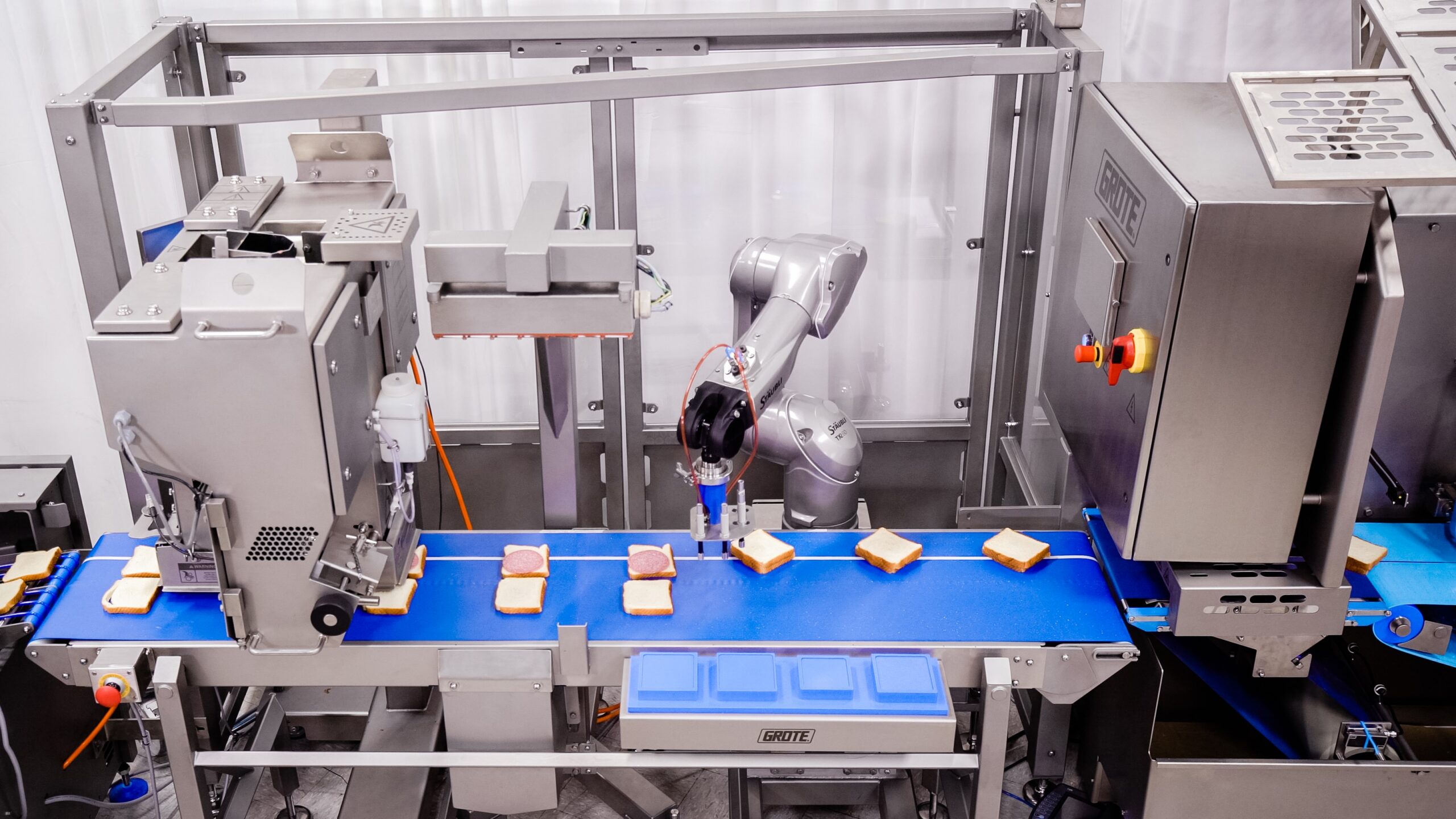 Multiple pizzas with sauce moving through a sauce applicator machine.