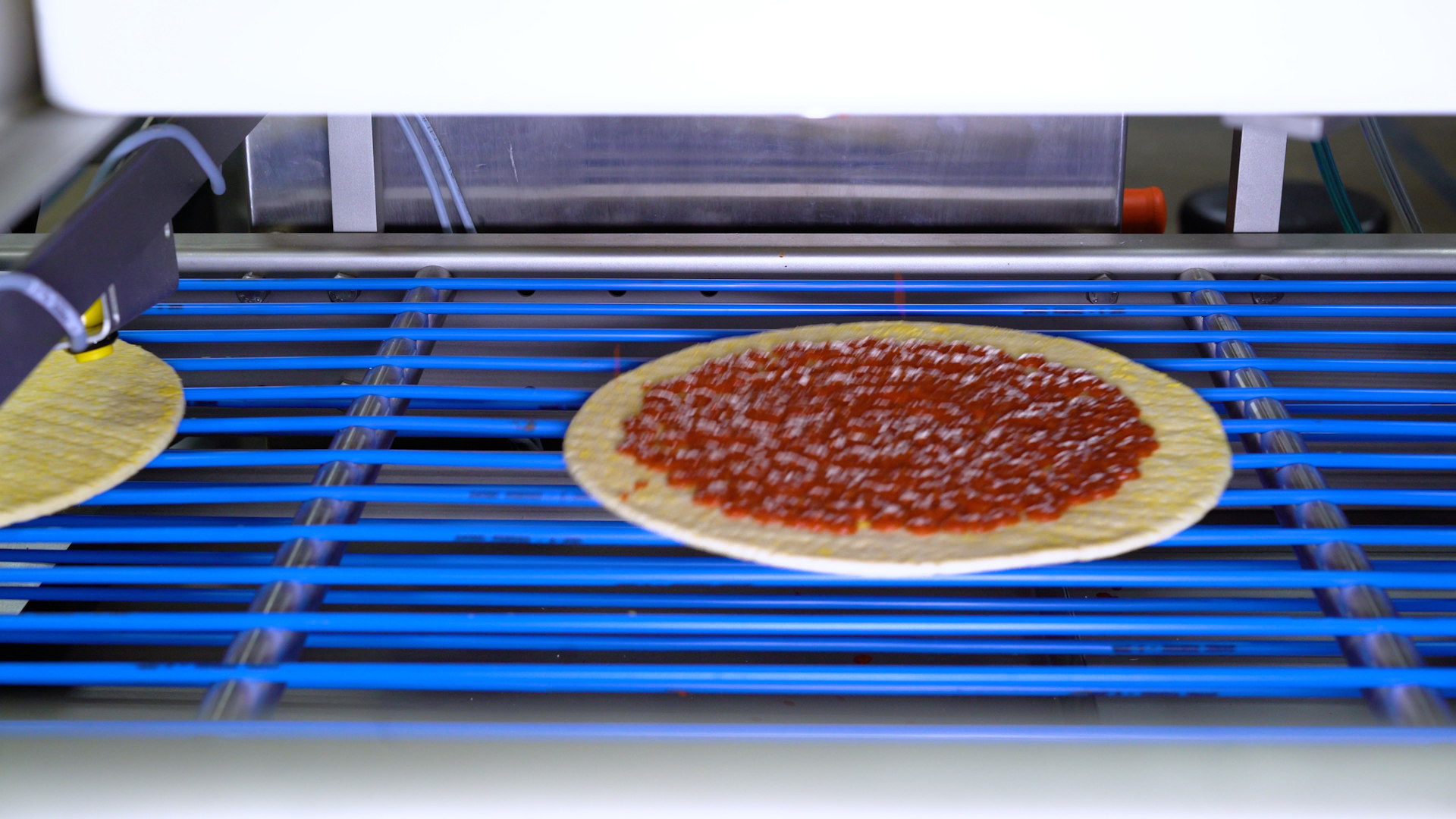 Una pizza moviéndose por una cinta transportadora en una máquina aplicadora de salsa de pizza. Una pizza moviéndose por una cinta transportadora en una máquina aplicadora de salsa de pizza.
