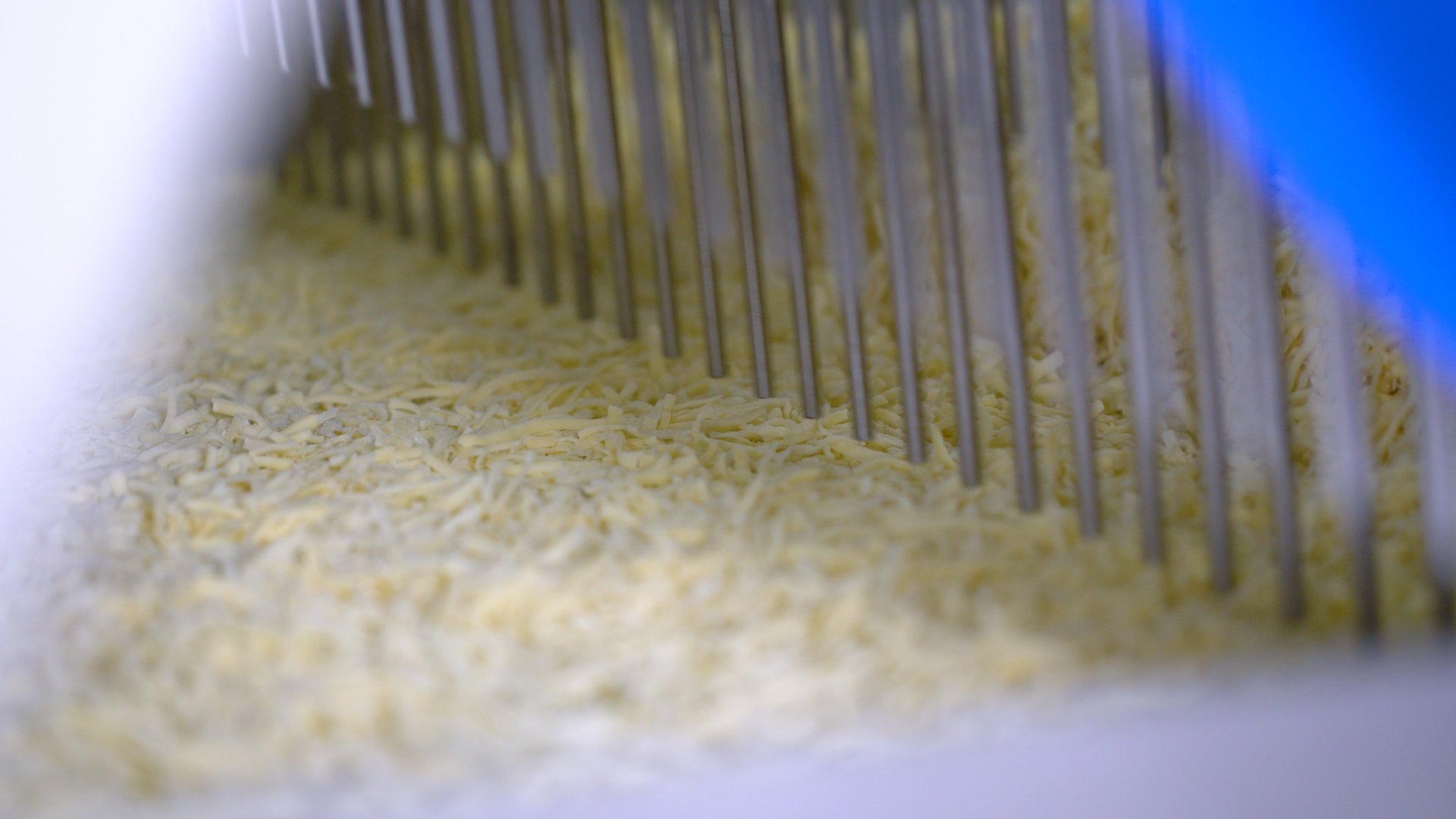 A close up of cheese moving through a pizza topping applicator.